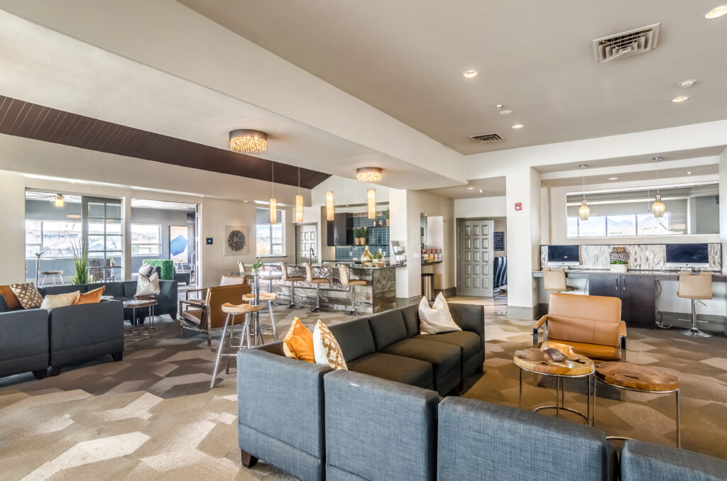 Clubhouse lounge with sofas and table, kitchen, and computer stations