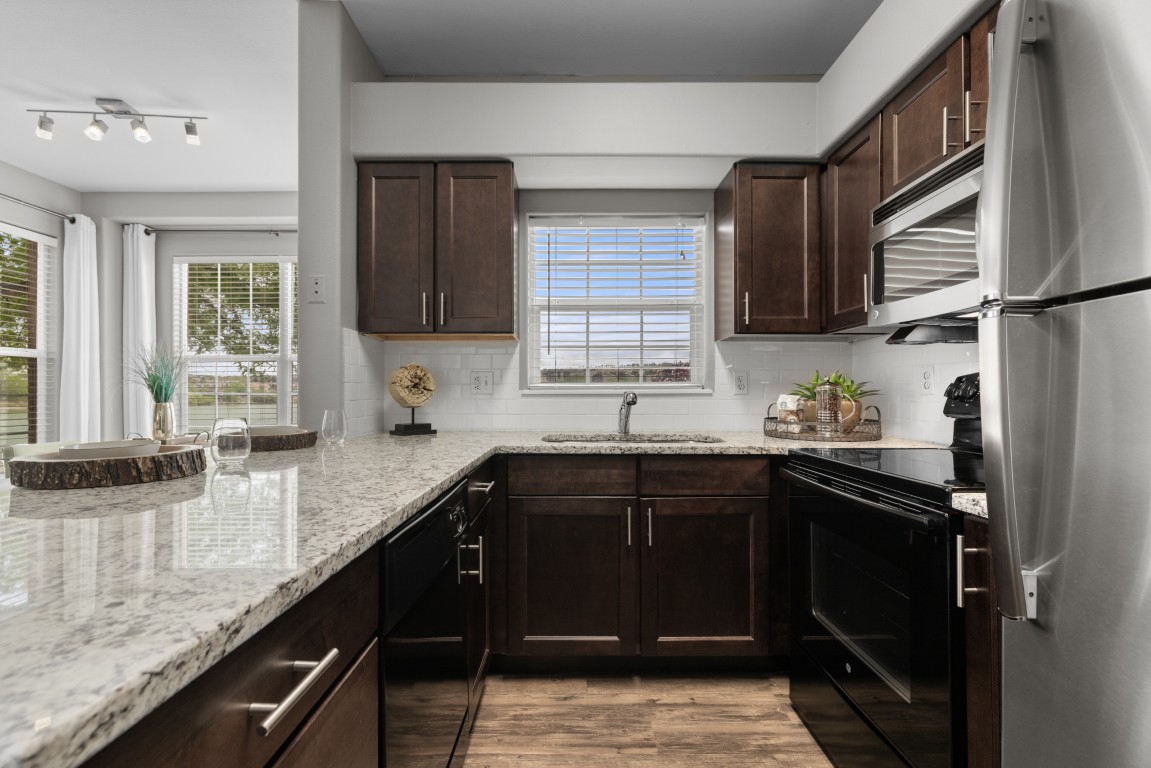 A modern kitchen with dark wood cabinets, granite countertops, and stainless steel appliances.